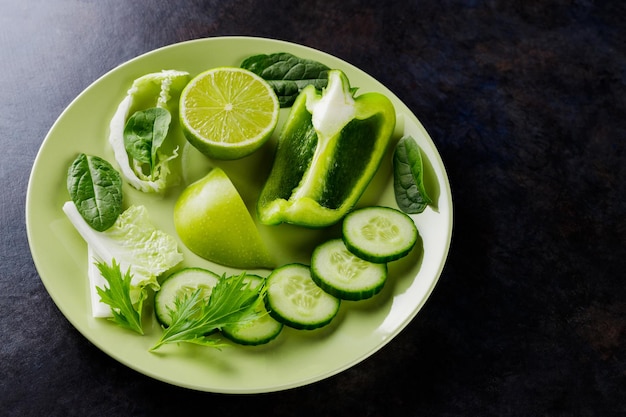 Verduras y frutas orgánicas sobre un fondo oscuro. Comida de dieta verde en un plato. Comida sana. Vista superior. Copia espacio