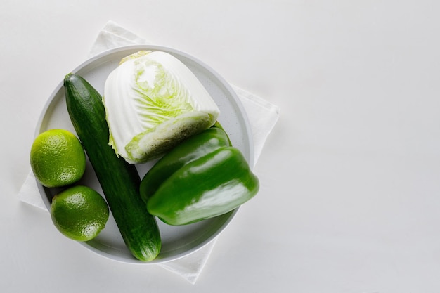 Verduras y frutas en un plato blanco. Pepino, repollo, pimiento y limón sobre una mesa blanca. Vista superior. Copia espacio