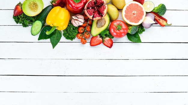 Verduras y frutas sobre un fondo de madera blanca. Melón, fresas, patatas, kiwi, granada, cítricos, aguacates. Vista superior. Espacio libre para su texto.