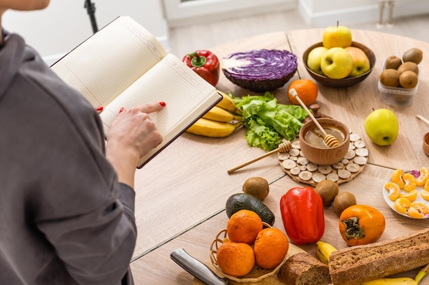 Foto verduras y frutas verdes frescas y saludables en la mesa de madera, dieta, fitness y estilo de vida activo y saludable. mujer con bloc de notas.