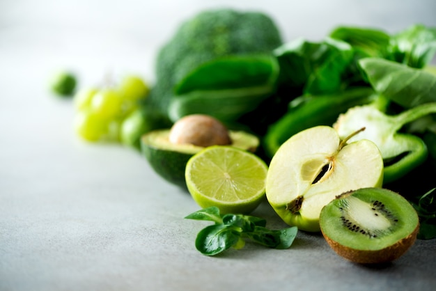 Verduras y frutas verdes orgánicas en fondo gris. Manzana verde, lechuga, pepino, aguacate, col rizada, lima, kiwi, uvas, plátano, brócoli.