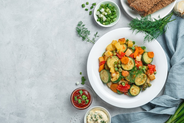 Verduras guisadas saludables en un plato blanco sobre un fondo gris. Vista superior, espacio de copia.