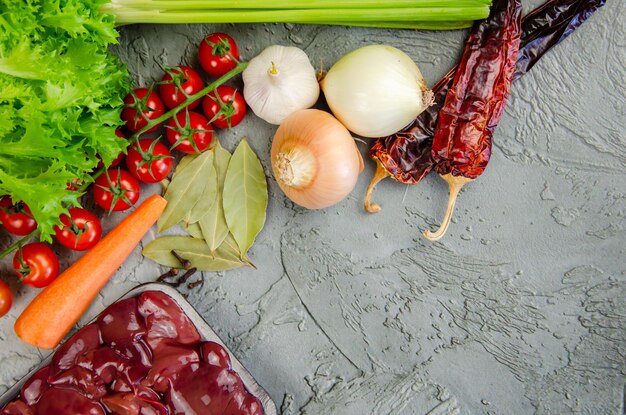 Verduras de hígado de pollo crudas y especias para hacer paté sobre un fondo gris de hormigón texturizado