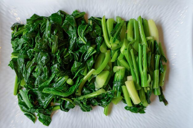 Foto las verduras kale chinas tailandesas deslizadas y hervidas separadas se colocaron en el rectángulo blanco en la mesa de madera