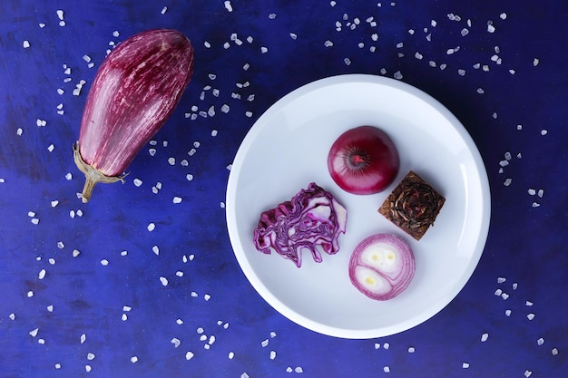 Verduras moradas en un plato blanco Composición de verduras sobre un fondo azul con cristales de sal marina Vista de cierre desde arriba