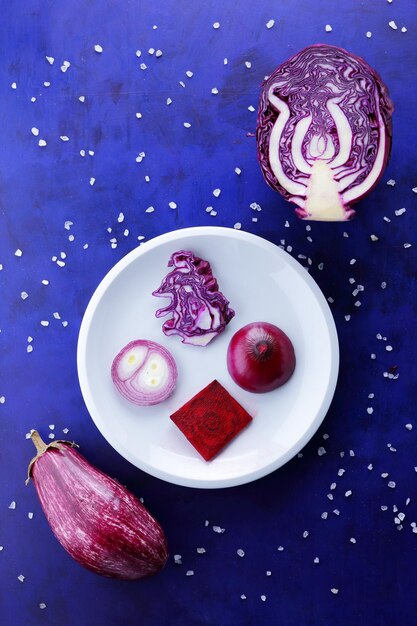 Verduras moradas en un plato blanco Composición de verduras sobre un fondo azul con cristales de sal marina Vista de cierre desde arriba