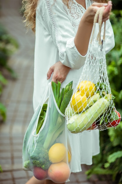 Verduras. Mujer en vestido blanco llevando bolsas con diferentes verduras