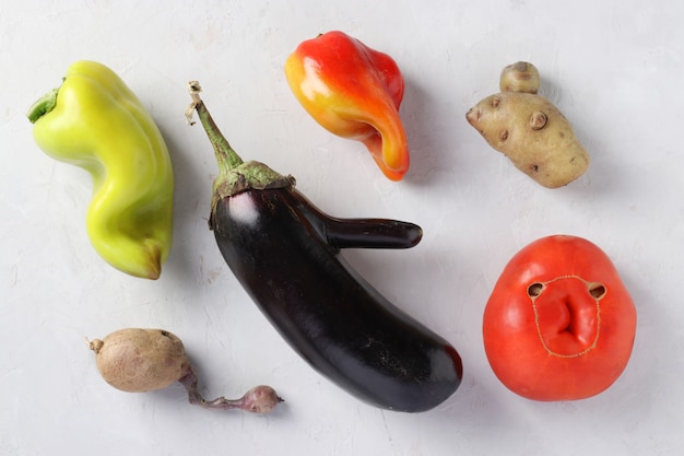 Verduras orgánicas feas de moda: patatas, pimientos, berenjenas y tomates sobre fondo gris, concepto de comida fea, formato horizontal, vista desde arriba