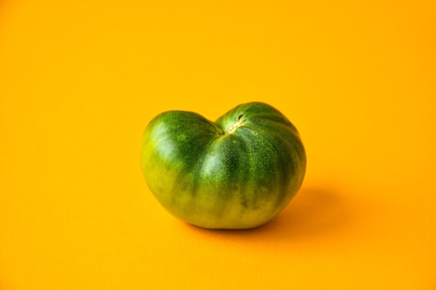 Verduras orgánicas feas de moda. Tomate verde sobre fondo amarillo. Cocinar el concepto de comida fea. Vista superior. Copie el espacio para el texto.