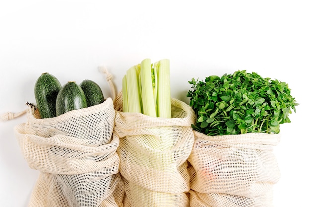 Verduras orgánicas y verduras frescas en bolsas de productos reutilizables sobre fondo blanco.