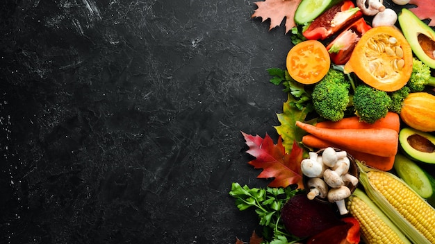 Verduras de otoño sobre un fondo de piedra negra Calabaza tomates maíz pepino cebolla zanahoria Comida de otoño Vista superior Espacio de copia libre