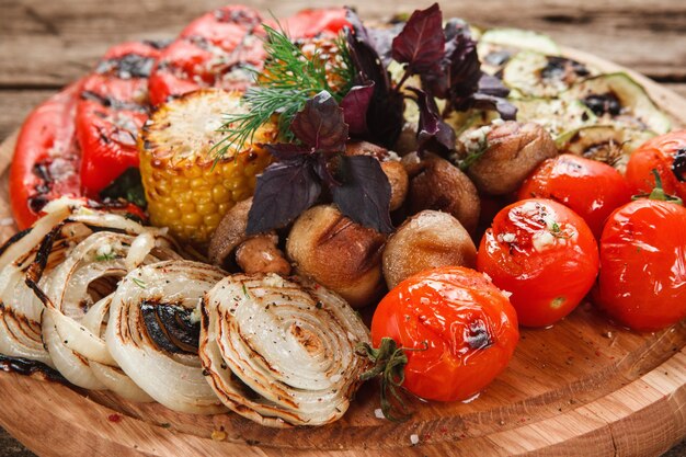 Verduras a la parrilla deliciosas. Tomates, pimiento rojo, cebolla, calabacín, maíz y champiñones decorados con albahaca, vista de cerca.