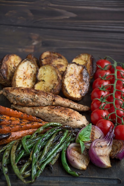 Foto verduras a la parrilla sobre una tabla para cortar sobre un fondo oscuro de la madera. fondo de madera oscura