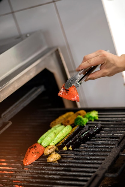 Verduras a la parrilla tomates maíz berenjena calabacín champiñones pimientos dulces se preparan en una máquina de parrilla profesional Chef asa verduras en la cocina del restaurante