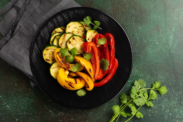 Verduras a la parrilla trozos de calabacín, pimiento rojo y amarillo y ramo de cilantro en un plato, ensalada en parrilla sobre carbón. Concepto de barbacoa.