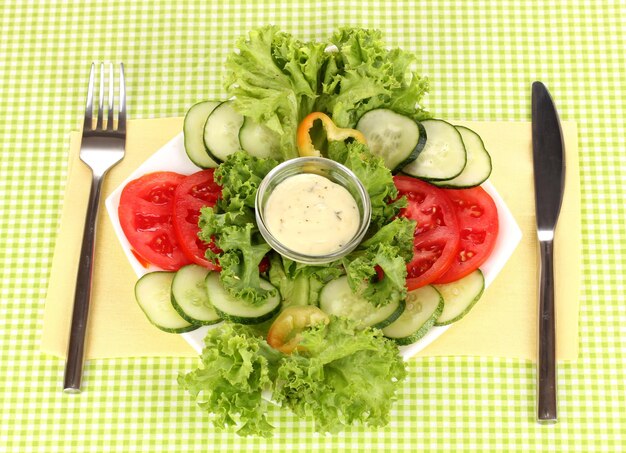 Foto verduras picadas y salsa en un plato sobre mantel verde