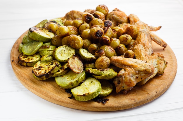 Verduras a la plancha y alitas de pollo en el plato de madera.