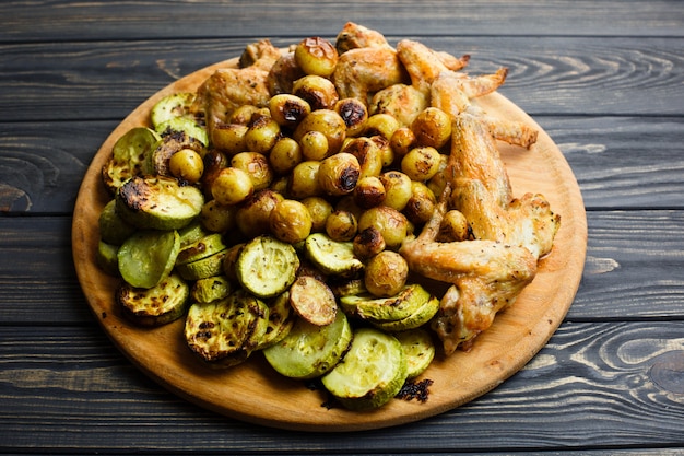 Verduras a la plancha y alitas de pollo en el plato de madera.