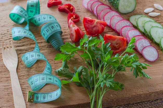 Verduras en rodajas y cinta métrica verde sobre tablero de madera