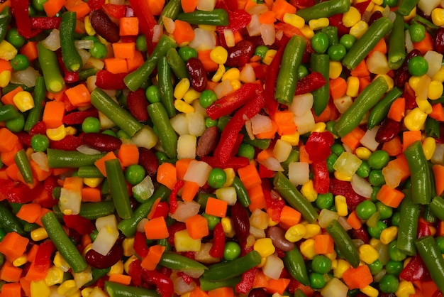 Verduras en rodajas, maíz, frijoles, guisantes, zanahorias, pimientos dulces de fondo.