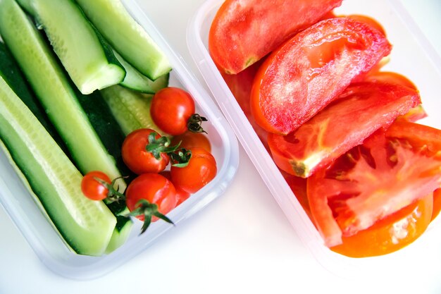 Verduras en rodajas en recipientes de plástico sobre un fondo blanco. Los pepinos y los tomates están en contenedores.