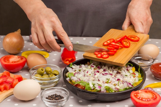 Verduras en rodajas en una sartén. Manos poner tomates en sartén