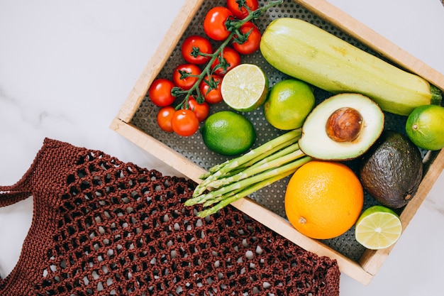 Verduras sanas frescas en caja de madera y bolso de compras del eco en el fondo de mármol blanco