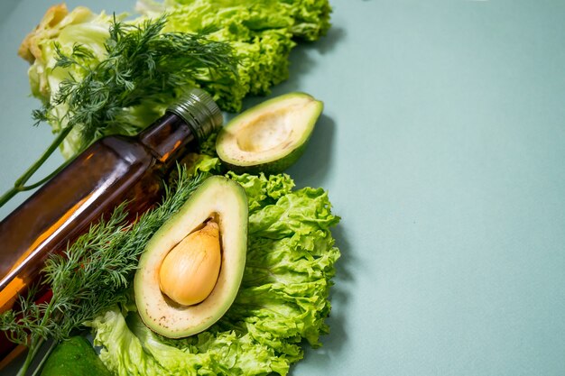 Verduras verdes con vidrio boutle de aceite sobre un fondo verde Verduras de ensalada Romano de aguacate Vista superior Sin plástico Concepto de dieta saludable