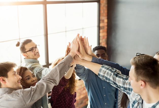 Vereinte Mitarbeiter, die mit den Händen zusammen im Loft-Büro stehen, erfolgreiches Projekt feiern, Platz kopieren