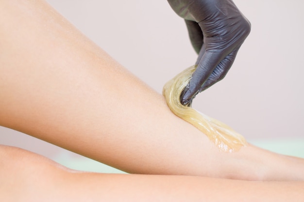 Verfahren der Haarentfernung am Bein schöne Frau mit Zuckerpaste oder Wachshonig und schwarze Handhand