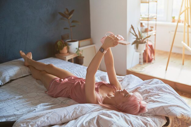 Verführerische langbeinige Frau macht Selfie mit modernem Smartphone auf großem Bett