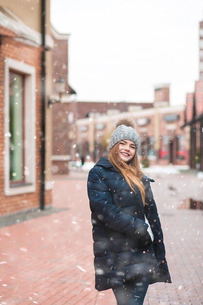 Verführerische rothaarige Frau, die während des Schneefalls auf der Feiertagswintermesse spaziert