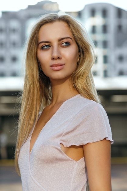 Verführerisches blondes Model mit perfekter Haut und langen Haaren posiert auf der Straße. Outdoor-Modekonzept