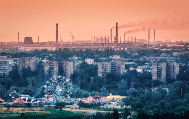 Vergnügungspark mit Riesenrad und Gebäuden in Mariupol Ukraine vor dem Krieg Stahlwerk bei Sonnenuntergang Stahlwerk mit Schornsteinen Stahlwerk Eisenwerk Schwerindustrie Hüttenkombinat