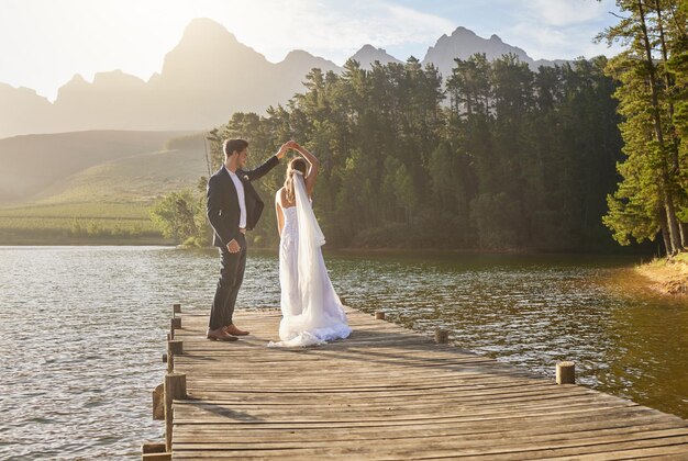 Verheirateter Tanz und ein Paar auf einem Pier über einem See in der Natur mit einem Wald im Hintergrund nach einer Zeremonie Hochzeitsliebe oder Wasser mit einem Brautpaar zur Feier ihrer Hochzeit im Freien