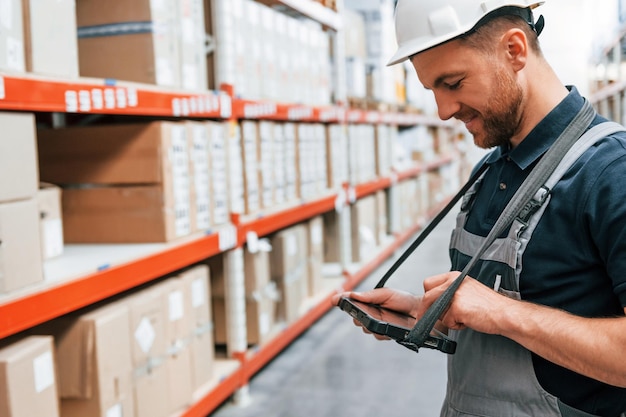 Verificación de datos en la tableta El empleado uniformado está trabajando en el almacenamiento durante el día