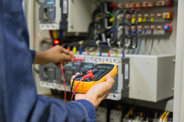 Verificador do trabalho do coordenador do eletricista que mede a tensão e a corrente da linha elétrica do poder no controle electical do armário.