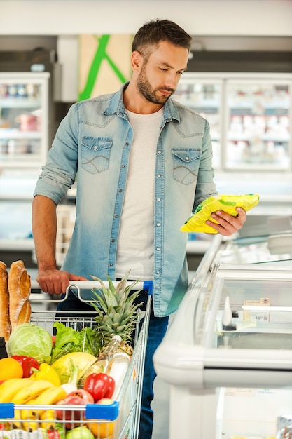 Foto verificando a data de validade. jovem confiante tirando comida da geladeira enquanto está em uma loja de alimentos