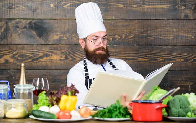 Verificando a lista de compras Vitamina homem usa utensílios de cozinha Dieta com alimentos orgânicos Legumes frescos concentrado homem cozinhando na cozinha Chef profissional em uniforme de cozinheiro Comida saudável e vegetariana