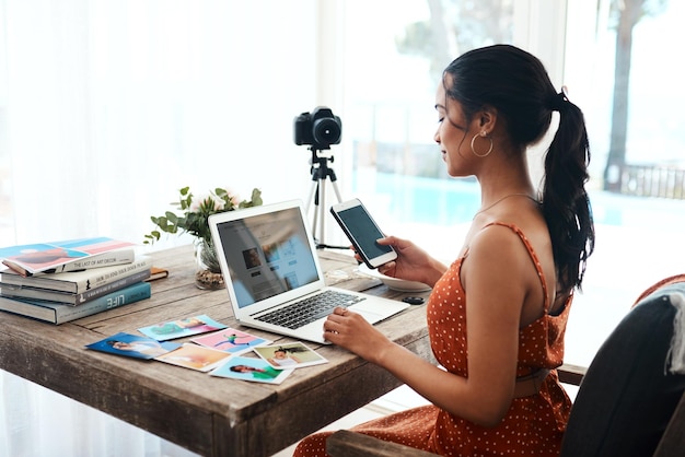 Verificando minhas mensagens de texto Foto recortada de uma jovem empresária atraente sentada e usando seu celular enquanto bloga de seu laptop