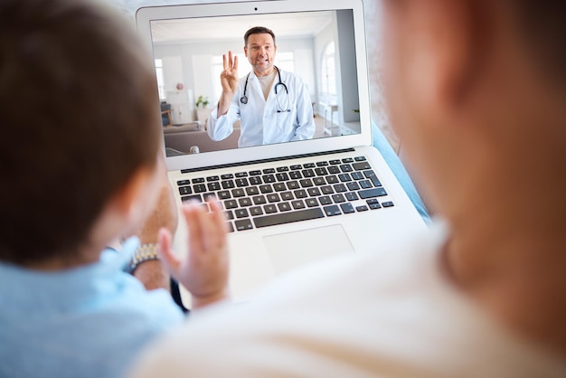 Verifique com o gp local. Foto de um menino irreconhecível e seu pai usando um laptop para uma videochamada em casa.