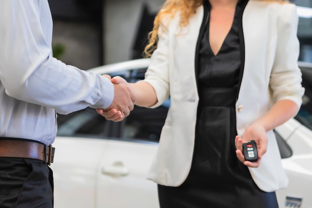 Verkäuferin des Frauen-Handshake-Fahrzeugs mit Kunden, die neue Autos im Ausstellungsraum präsentieren.