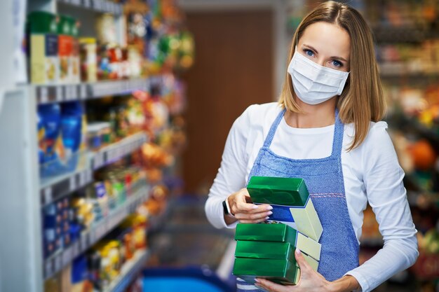 Verkäuferin, die in medizinischer Maske im Lebensmittelgeschäft arbeitet