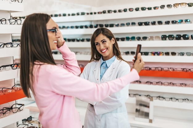 Verkäuferinnen und Kunden im mittleren Alter, die sich für neue Brillen in einem modernen Optikgeschäft entscheiden. Shopping-Konzept.