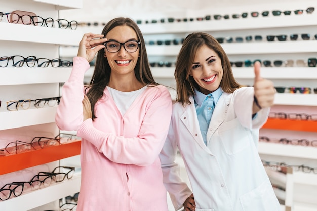 Verkäuferinnen und Kunden im mittleren Alter, die sich für neue Brillen in einem modernen Optikgeschäft entscheiden. Shopping-Konzept.