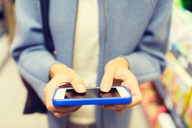 Foto verkauf, einkaufen, konsum und personenkonzept - nahaufnahme einer frau mit smartphone, die lebensmittel auf dem markt auswählt und kauft