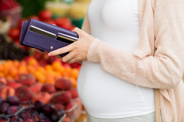 verkauf, einkaufen, schwangerschaft und personenkonzept - nahaufnahme einer schwangeren frau mit brieftasche und kreditkarten, die lebensmittel auf dem straßenmarkt kaufen