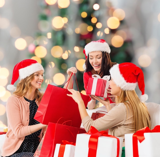 verkauf, winterferien und personenkonzept - lächelnde junge frau in weihnachtsmannmütze mit geschenken und einkaufstüten über weihnachtsbaum beleuchtet hintergrund