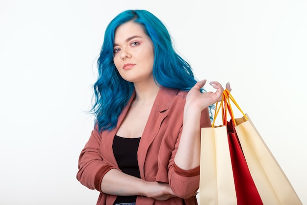 Verkaufs-, Shopaholic- und Verbraucherkonzept - schönes Mädchen mit blauem Haar, das mit Einkaufstaschen auf weißem Hintergrund steht.