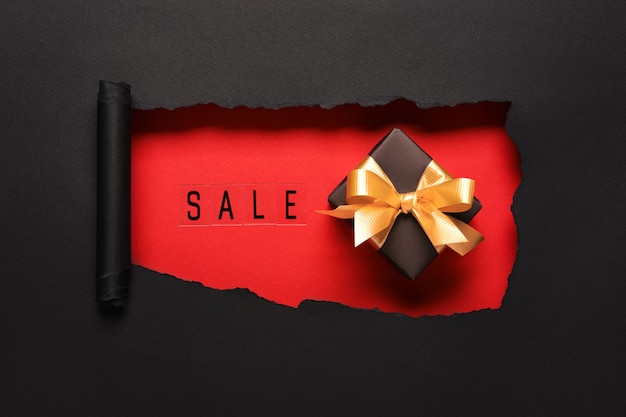 VERKAUFStext auf rotem Lochhintergrund mit schwarzer Geschenkbox und goldenem Bogen. Shopping Rabattaktion.